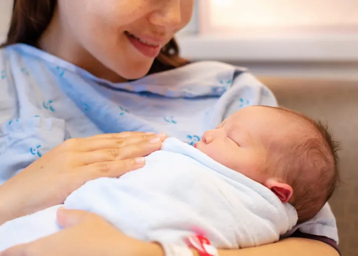 A mother in a hospital gown cradling her sleeping newborn baby